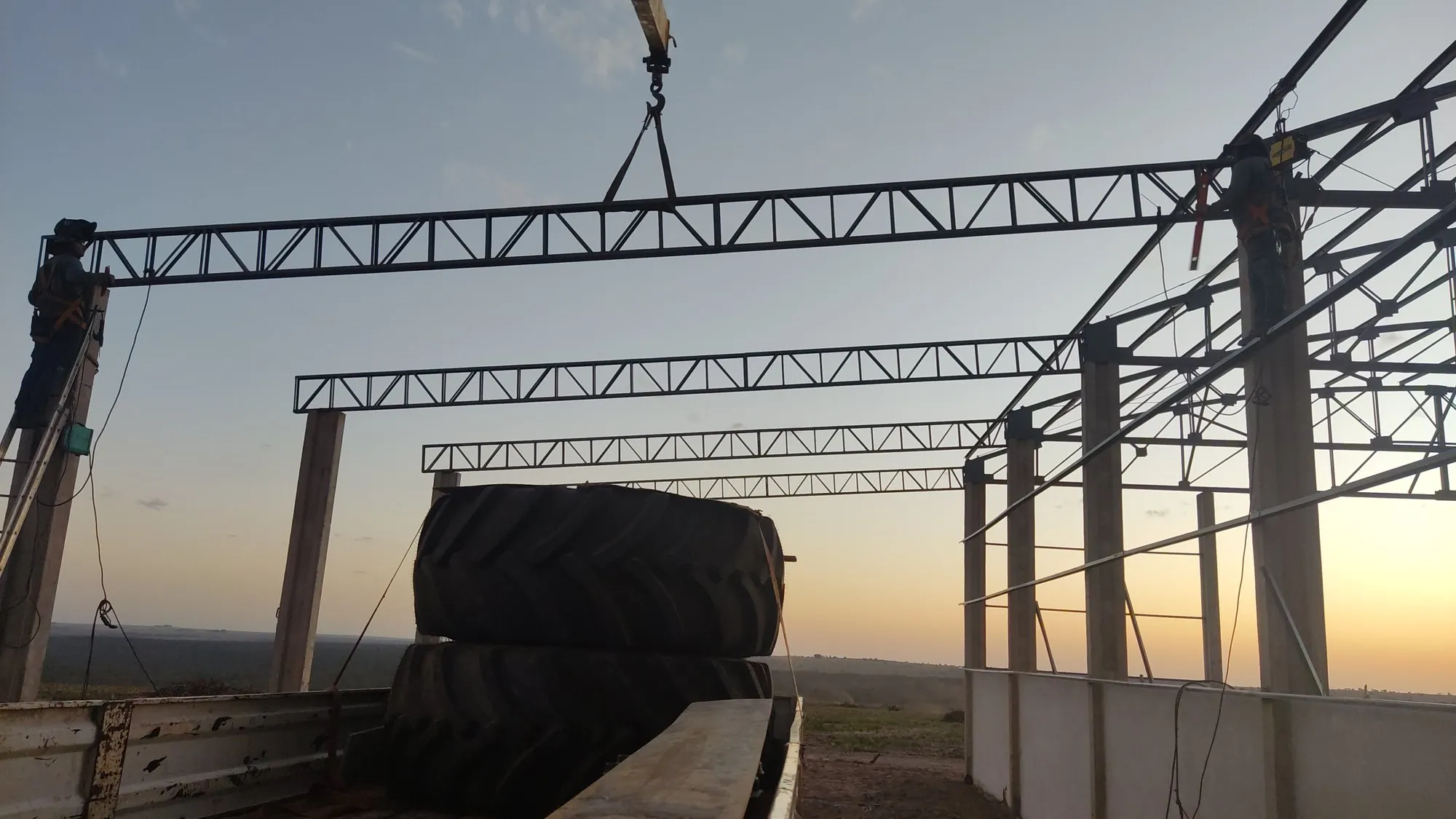 Tesoura metálica treliçada suspensa por guindaste durante içamento em obra de galpão — MR Serralheria