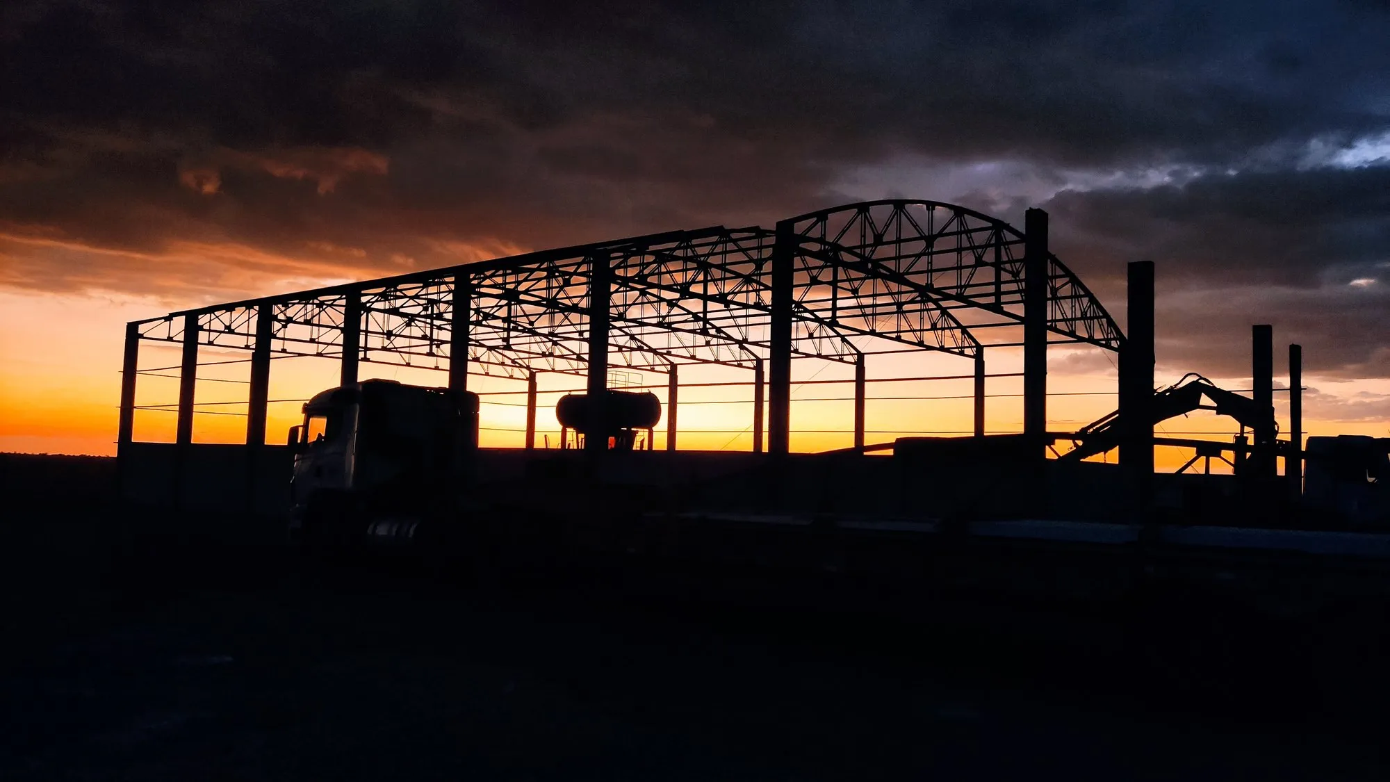 Silhueta da estrutura metálica em arco de galpão rural ao pôr do sol — MR Serralheria, Norte do Paraná